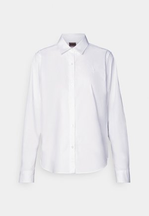 Chemise blanche à manches longues, boutonnée, fabriquée en coton. Comprend un col classique et une broderie de marque discrète sur la poitrine. Texture lisse.