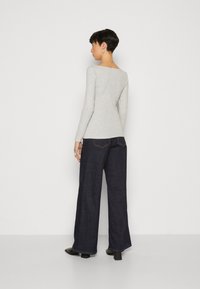 Hellgrau longsleeve Oberteil mit Bootsausschnitt, kombiniert mit dunkelblauen weit geschnittenen Jeans. Glatte Textur, tailliert, locker geschnitten unten.