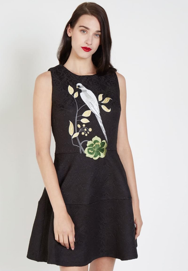 Vestido negro sin mangas con bordados de flores y pájaros en blanco, verde y amarillo, con un diseño texturizado y falda acampanada.