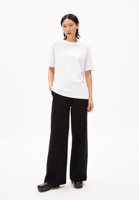 T-shirt blanc oversize, manches courtes, assorti à un pantalon noir à jambes larges et des sabots noirs à clous argentés. Design minimaliste, couleurs unies.