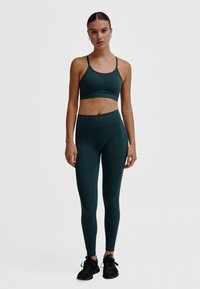 Donkergroene sportbeha en hooggetailleerde leggings gemaakt van gestructureerde stof. De outfit heeft dunne bandjes en een aansluitend silhouet.