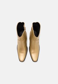 Bottines en cuir doré avec un bout pointu, une tige incurvée, des fermetures éclair latérales et une finition métallique lisse.