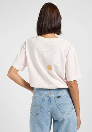 T-shirt cropped rosa chiaro con grafica "BEACH" in bianco e un accento rotondo beige. Tessuto di cotone morbido, maniche corte, vestibilità rilassata.