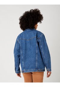 Džínová bunda v středně modré barvě, se klasickým límcem, dlouhými rukávy, knoflíkovým zapínáním a uvolněným střihem s obšitím.