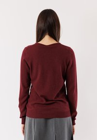 Maglione in lana borgogna con maniche lunghe e orlo a coste. Presenta un colletto rotondo e una texture morbida e leggermente pelosa.