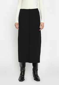 Zwarte midi rok met een rechte snit, hoge taille en een middelste achternaad. Gepaard met een nauwsluitend wit shirt met lange mouwen en hoge zwarte laarzen.
