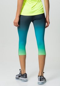 Legginsy typu capri z gradientowym wzorem przechodzącym od czerni do teal i zieleni, wykonane z elastycznego materiału, zestawione z czarnymi butami sportowymi.
