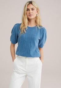 Top corto de manga corta en azul claro con patrón texturizado en chevron y escote redondeado, combinado con pantalones blancos de cintura alta.