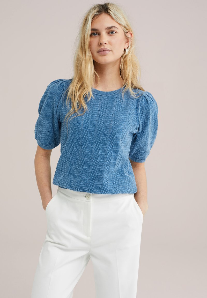 Top corto de manga corta en azul claro con patrón texturizado en chevron y escote redondeado, combinado con pantalones blancos de cintura alta.