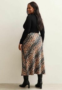 Svart långärmad topp i kombination med en flödande, mönstrad midiklänning med stora beige prickar på svart bakgrund, kompletterad med knähöga svarta stövlar.