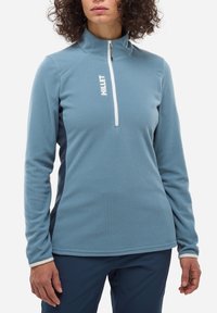 Pullover en polaire bleu texturé avec demi-zip, présentant des accents de logo blancs et des panneaux latéraux sombres contrastants. Manches longues.
