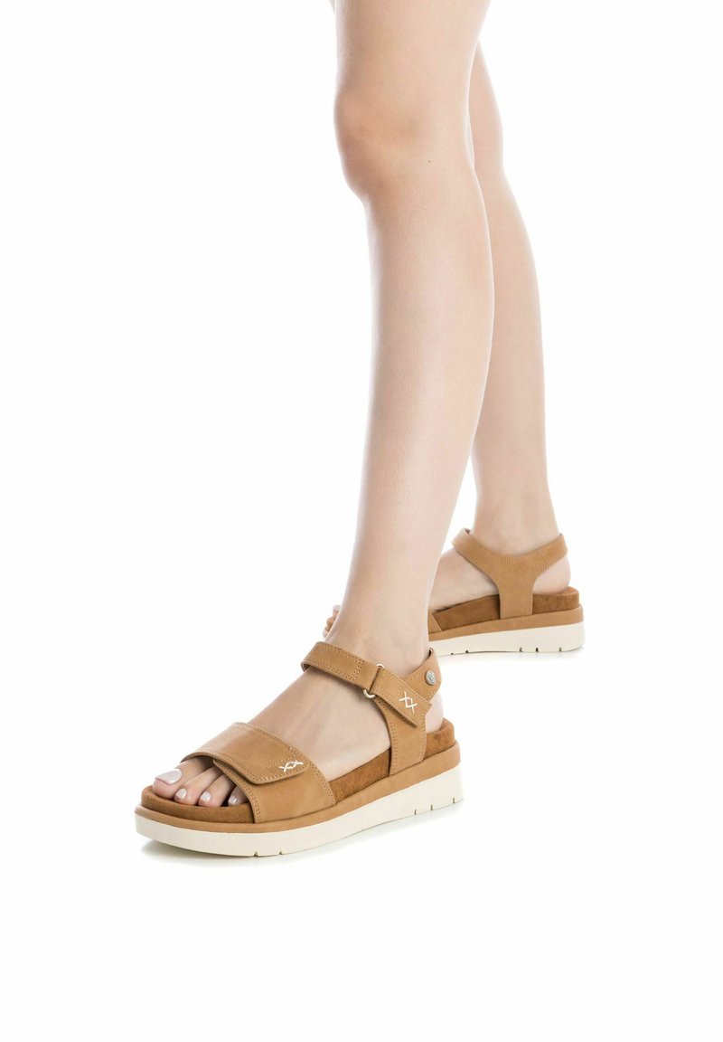 Sandalias de cuero marrón con correas ajustables, suelas acolchadas, suelas de goma y costuras decorativas. Diseño de talón cerrado y punta abierta.