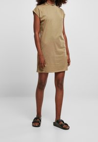 Khaki sukienka z krótkim rękawem i okrągłym dekoltem, charakteryzująca się luźnym krojem i gładką fakturą. W zestawieniu z czarnymi sandałami na płaskiej podeszwie.