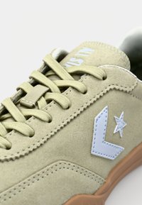 Adidași din piele intoarsă într-o nuanță bej deschis, cu șireturi asortate, având un logo albastru și o stea pe lateral, și o talpă texturată gumă.