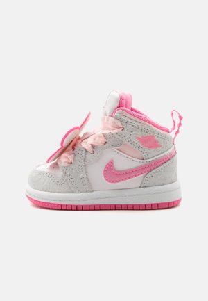 Baskets Nike pour tout-petits blanc et rose avec des panneaux texturés doux, un swoosh rose, des lacets en ruban et une semelle coussinée.