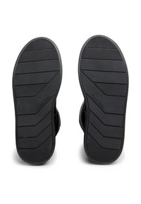 Suelas de zapatos de goma negra con patrones de banda de rodadura horizontales y diagonales. Presenta un logo "Calvin Klein" en relieve. Acabado suave y texturizado.