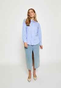 Svetlomodrá košeľa na gombíky s dlhými rukávmi, kombinovaná s svetlou rifľovou sukňou po kolená s predným rázporkom. Béžové lodičky s špičatou špičkou.