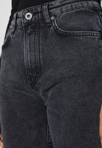 Jeans in denim nero con vita alta, chiusura a bottone e texture delicatamente consumata. Le tasche anteriori sono visibili su entrambi i lati.