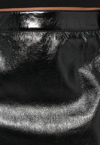 Tessuto similpelle nera con una superficie lucida e texture. Presenta una cintura liscia e una leggera piegatura per un tocco di dettaglio.