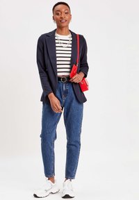 Navy blazer, gestreepte wit en zwarte top, hoge taille blauwe spijkerbroek, rode schoudertas, witte sneakers met zwarte accenten, zilveren sieraden.