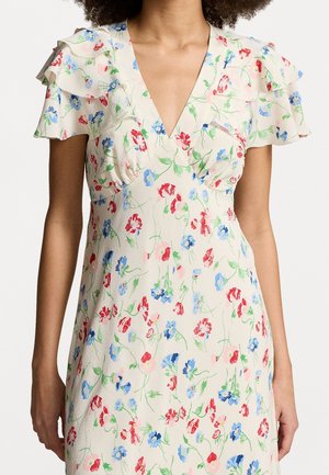 Mujer con vestido crema con escote en V, mangas acampanadas y estampado floral en rojo, azul y verde.