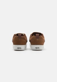 Smeđe zamšaste tenisice s bijelim gumiranim potplatima, s petnim trakama za povlačenje i logom "Vans Off The Wall" na peti.