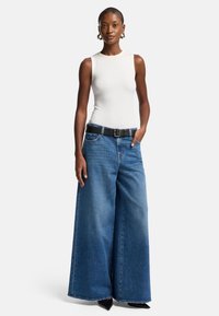 Breda ben blå denimjeans med hög midja, som har ett svart bälte, en åtsittande vit linne, och en slät textur.