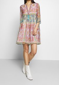 Vestido transparente con estampado floral colorido, escote en V, mangas tres cuartos y detalles de borlas. Combinado con botines blancos hasta el tobillo.