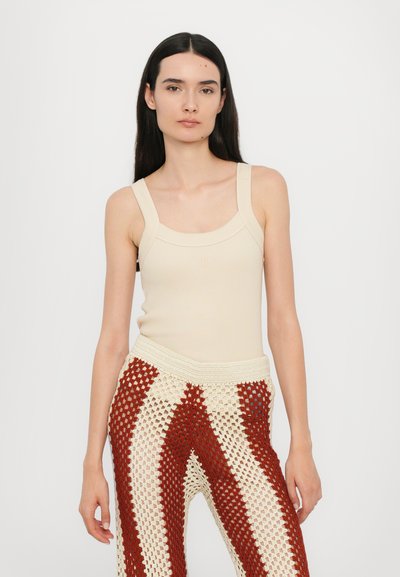 Beige geripptes Tanktop mit breiten Trägern, kombiniert mit rot-weißen gewebten Häkelhosen mit gestreiftem Muster und elastischem Taillenbund.