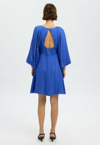 Vestido de satén azul con mangas largas y fluidas, cintura recogida y un corte en forma de llave en la parte posterior. Textura suave, dobladillo a la altura de la rodilla.