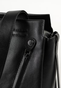 Zwarte leren tas met brede riem, metalen drukknoop en gestikte details op een gladde, gestructureerde oppervlakte.