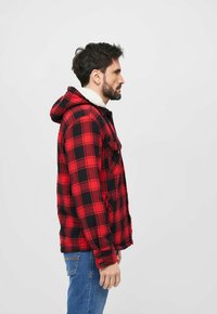 Rød og sort ternet flanneljakke med hætte og hvid pelskrave, med knaplukning ved ærmerne og en sidelomme.