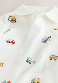 White polo shirt featuring colorful embroidered construction vehicles, including trucks and excavators, with a textured fabric and three-button placket.