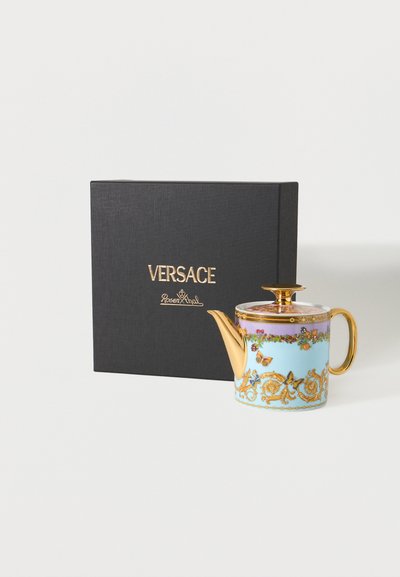 Τσαγιέρα με χρυσή λαβή, ρύγχος και καπάκι, διακοσμημένη με λουλουδένια και πεταλούδα σχέδια, εκτεθειμένη δίπλα σε μαύρο κουτί με τα λογότυπα Versace και Rosenthal.