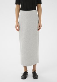 Grauer Maxirock aus weichem Stoff mit geradem Schnitt und ohne sichtbare Verschlüsse. Kombiniert mit einem gerippten schwarzen Oberteil und Schnürschuhen.