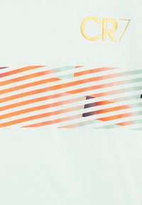 Svijetlozeleni sako s zlatnim logotipom "CR7". Pruge u narančastoj, ljubičastoj i mint boji stvaraju dinamičan uzorak na tkanini.