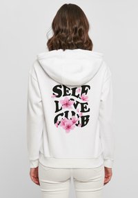 Fehér kapucnis pulóver fekete "SELF LOVE CLUB" felirattal, rózsaszín virágos díszítéssel. Puha anyagból készült, húzózsinóros kapucnival és bordás mandzsettákkal.