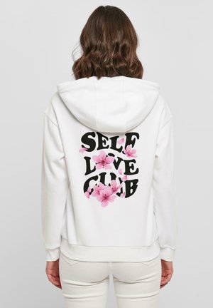 Valkoinen huppari, jossa on musta "SELF LOVE CLUB" -tuloste ja vaaleanpunaisia kukkakoristuksia. Pehmeää kangasta, nyörikaulus ja ribbireunat.