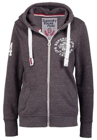 Sudadera gris con cremallera hecha de una tela texturizada. Presenta un gran estampado de logo, bolsillos tipo canguro y cordones en contraste en la capucha.