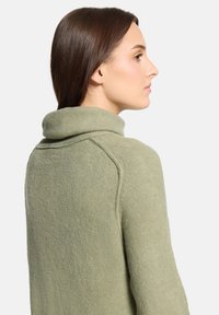 Pull vert clair à col montant, fabriqué en tissu doux. Présente une coupe décontractée et une texture côtelée au niveau du col et des manches.
