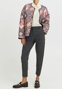 Farverig quiltet jakke med geometrisk mønster, kombineret med skræddersyede mørkegrå bukser og sorte loafers med guld accenter.