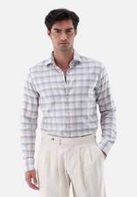 Helle, kariert Bluse mit lila und blauen Quadraten, langen Ärmeln und einem klassischen Kragen, kombiniert mit beigen, gefalteten Hosen.