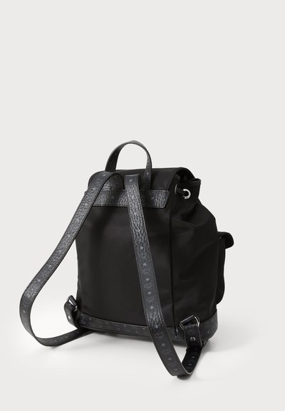 Mochila negra con correas y acentos de cuero texturizado, cierre de cordón y un asa en la parte superior, mostrada en ángulo sobre un fondo claro.