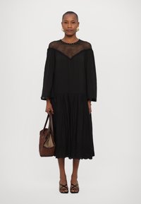 Musthave mustdress, millekaeluse ja pikkade varrukatega, millelt on tikkimisega äär. Kombineeritud punutud pruunist kotiga ja mustade rihmadega sandaalidega.