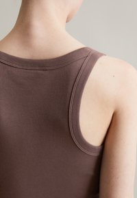 Braun geripptes Tanktop mit weiter Ausschnitt und schmalen Trägern, das eine weiche Textur und runde Armausschnitte aufweist.