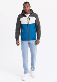 Giacca a blocchi di colore con corpo blu, maniche grigie e un pannello superiore bianco. Dotata di cappuccio, tasche con zip e polsini a coste.