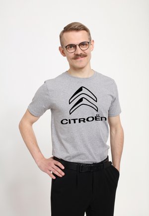 Šedé bavlněné tričko se vzorem černého loga Citroën a šípového designu. Nosí se s černými kalhotami a černým pásem. Jednoduchý, neformální design.