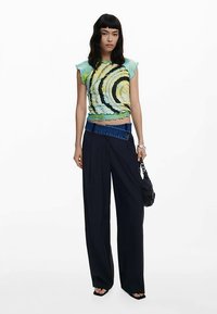 Crop top ajusté multicolore avec motifs ondulés ; pantalon large bleu marine ; ceinture en jean bleu ; sac à main noir ; texture lisse ; design sans manches.