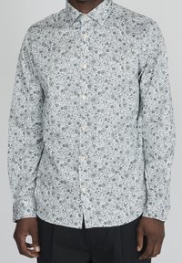 Vit långärmad skjorta med grönt blommönster. Har krage med knappar och knappar fram, med en figurnära silhuett.