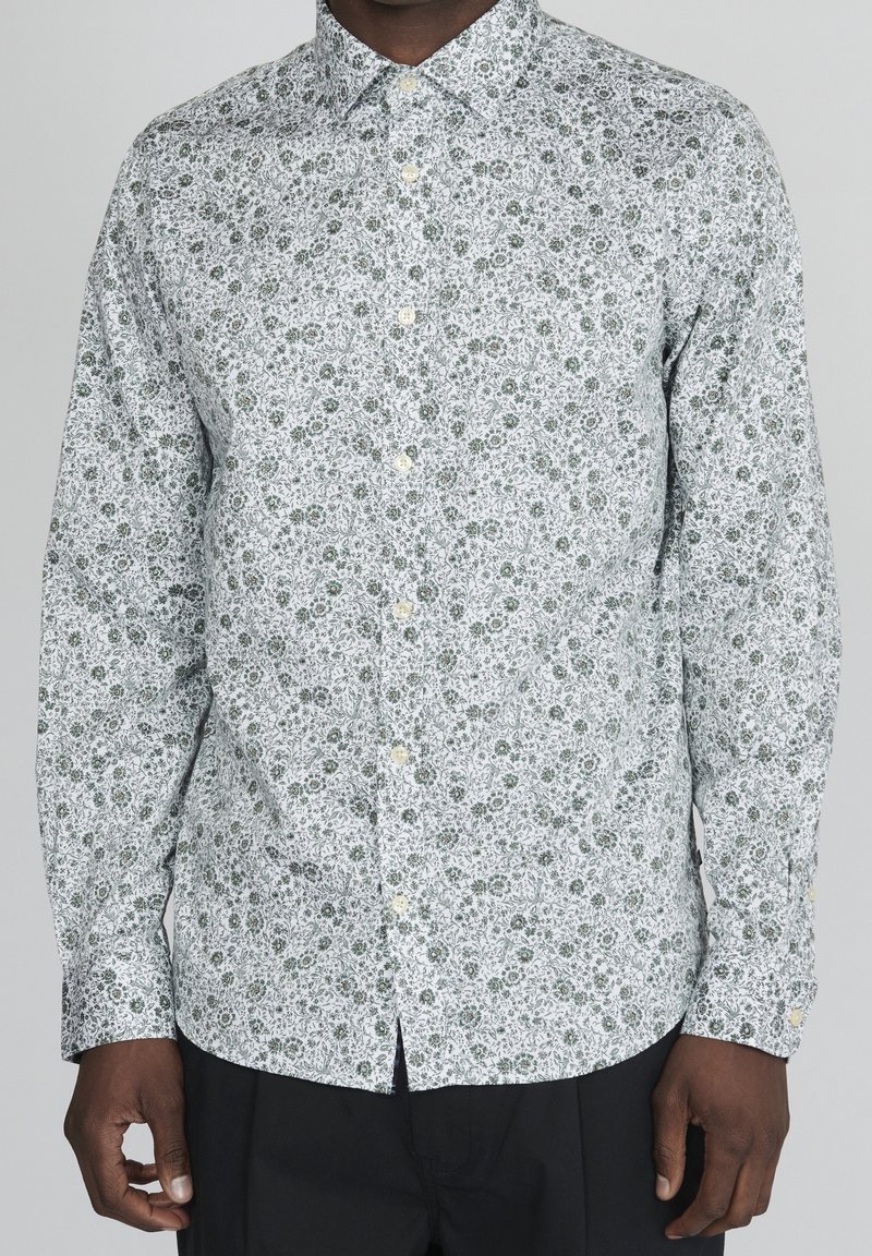 Vit långärmad skjorta med grönt blommönster. Har krage med knappar och knappar fram, med en figurnära silhuett.